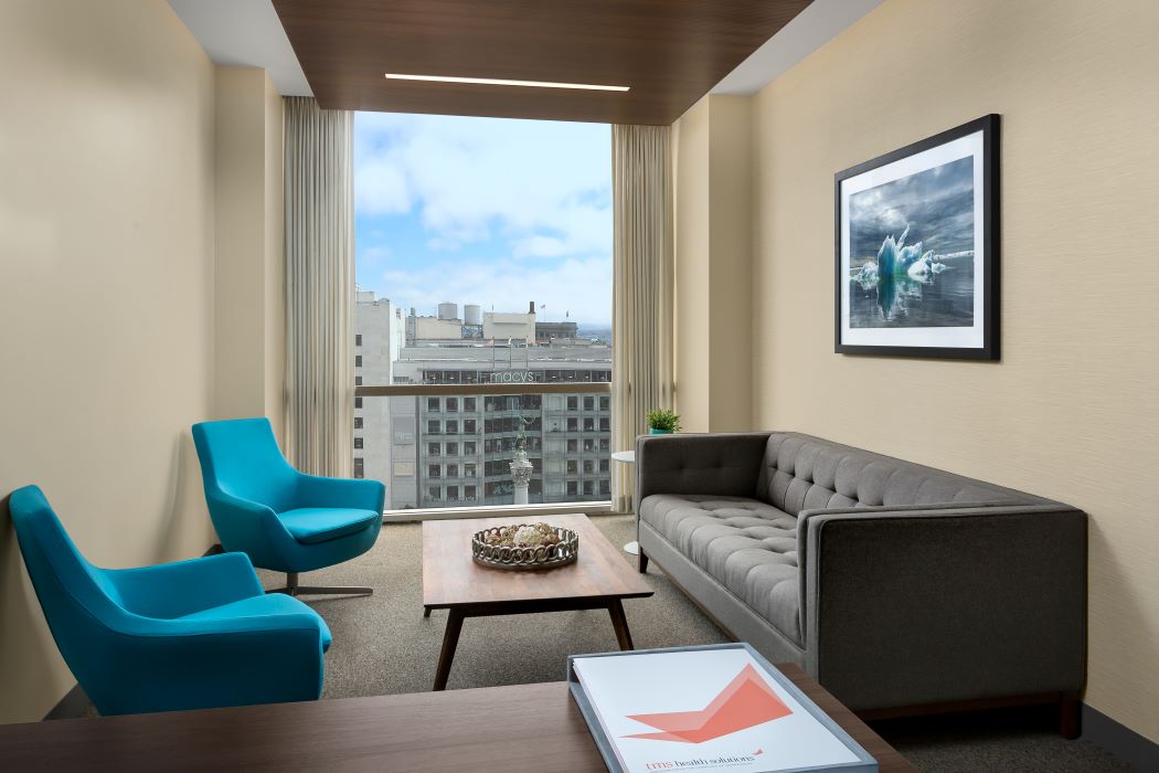Modern clinical office with turquoise chairs, gray sofa, and city skyline view through floor-to-ceiling windows