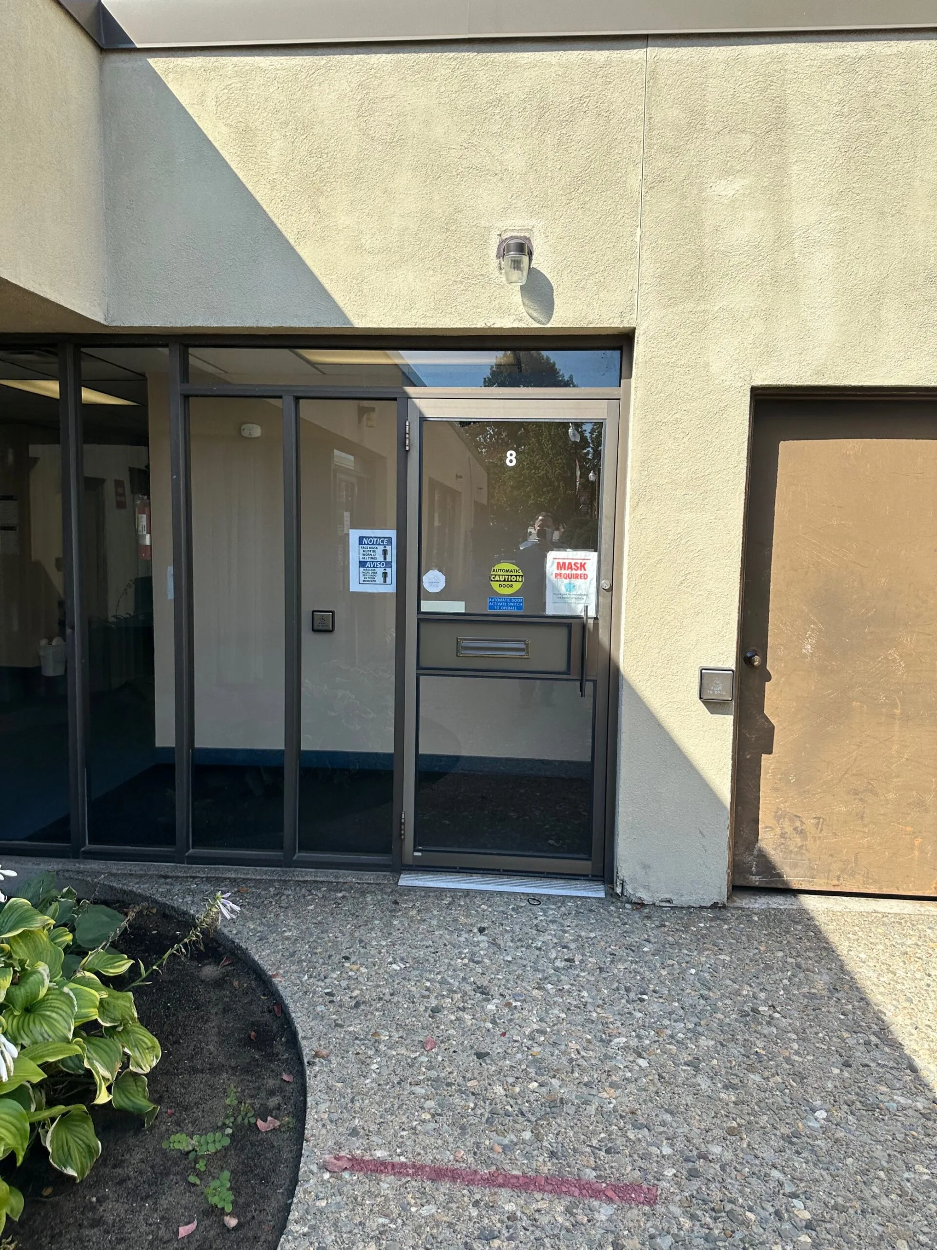Medical office entrance with glass door marked with unit number 8, no smoking sign, and mask required notices