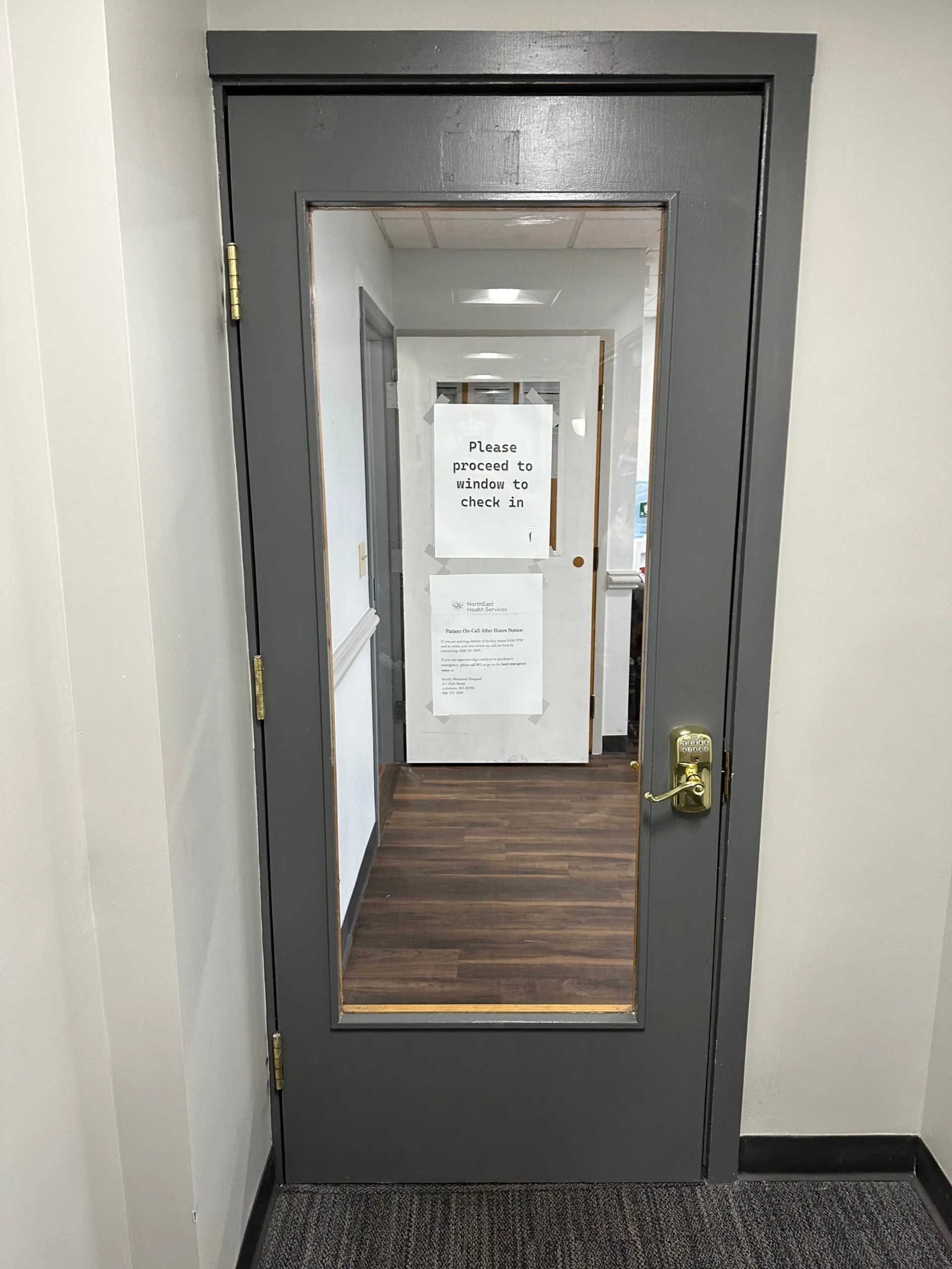 Gray door with glass window and sign reading 'Please proceed to window to check in'