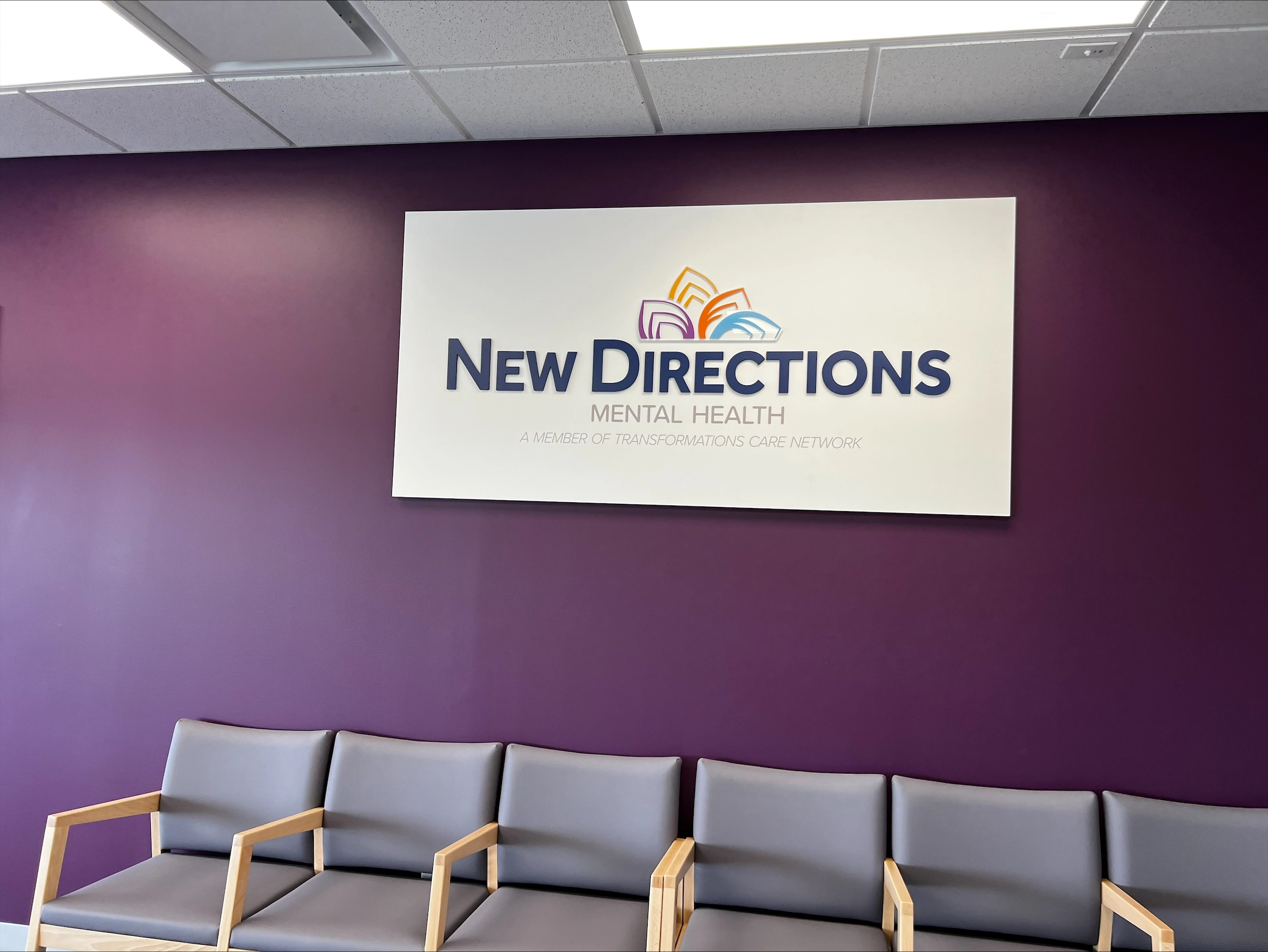 New Directions Mental Health signage on purple waiting room wall above gray seating