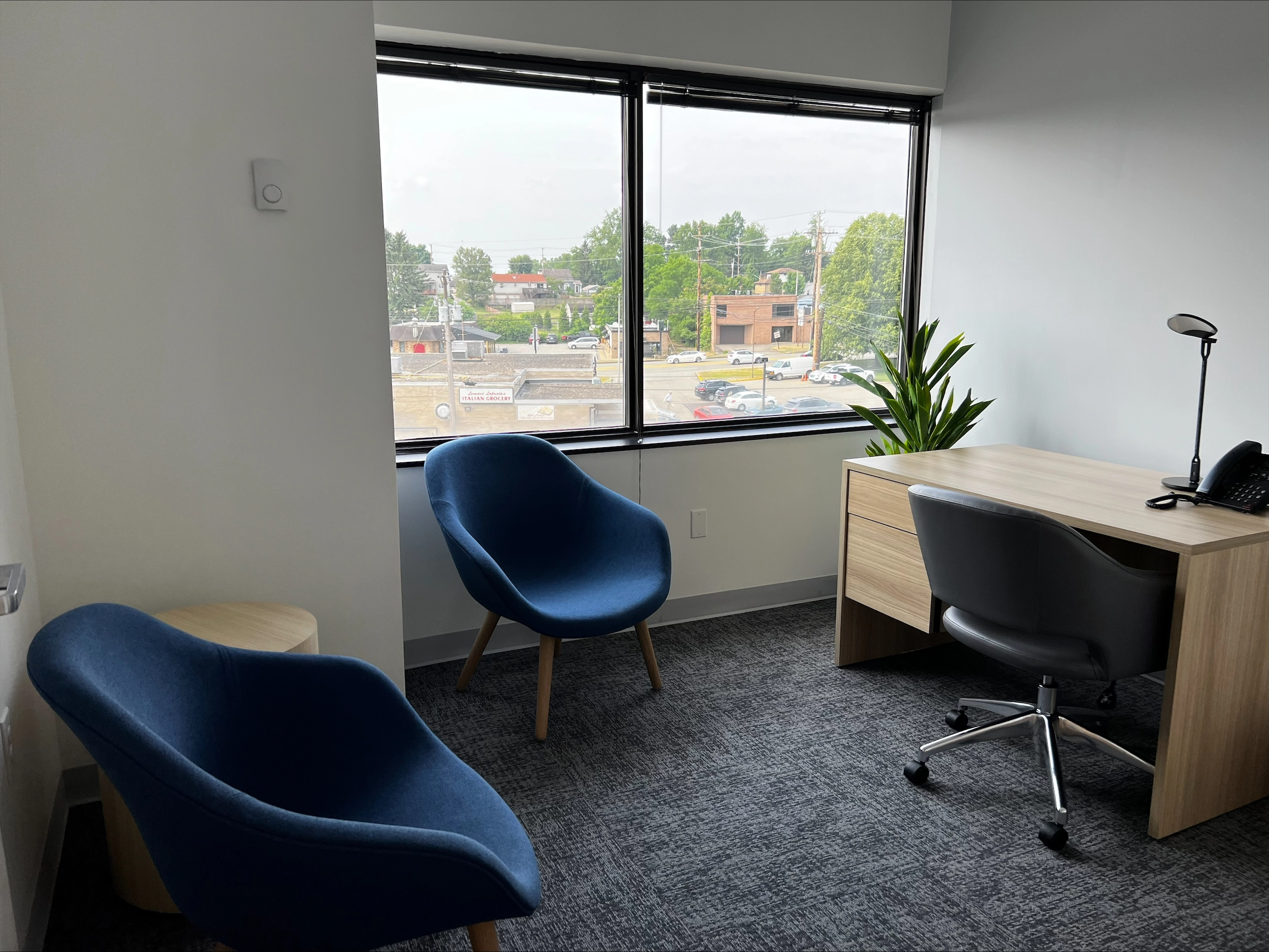 Office space with two blue chairs, desk, and large windows overlooking Monroeville