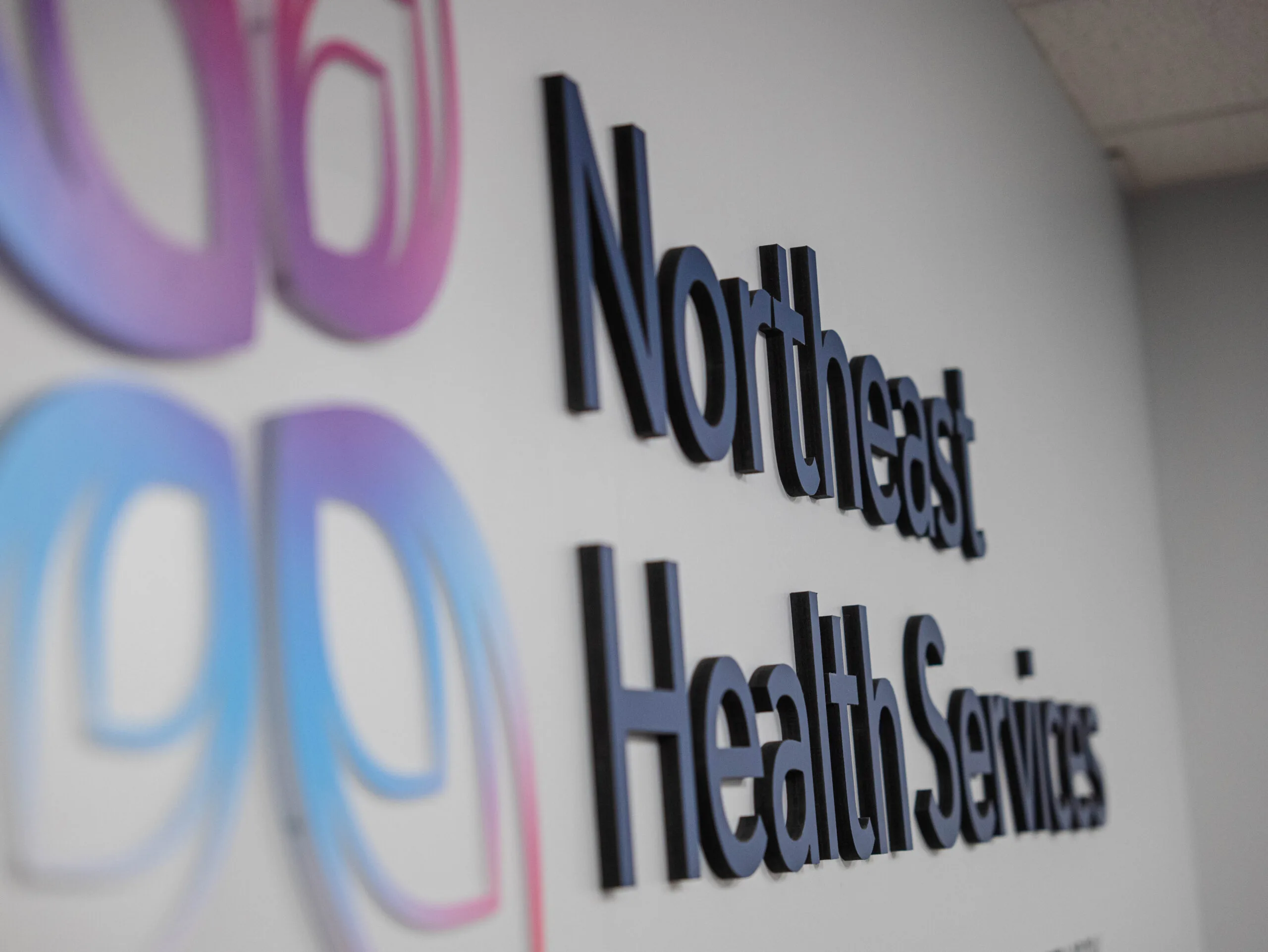Northeast Health Services wall signage in black text with purple and blue gradient logo