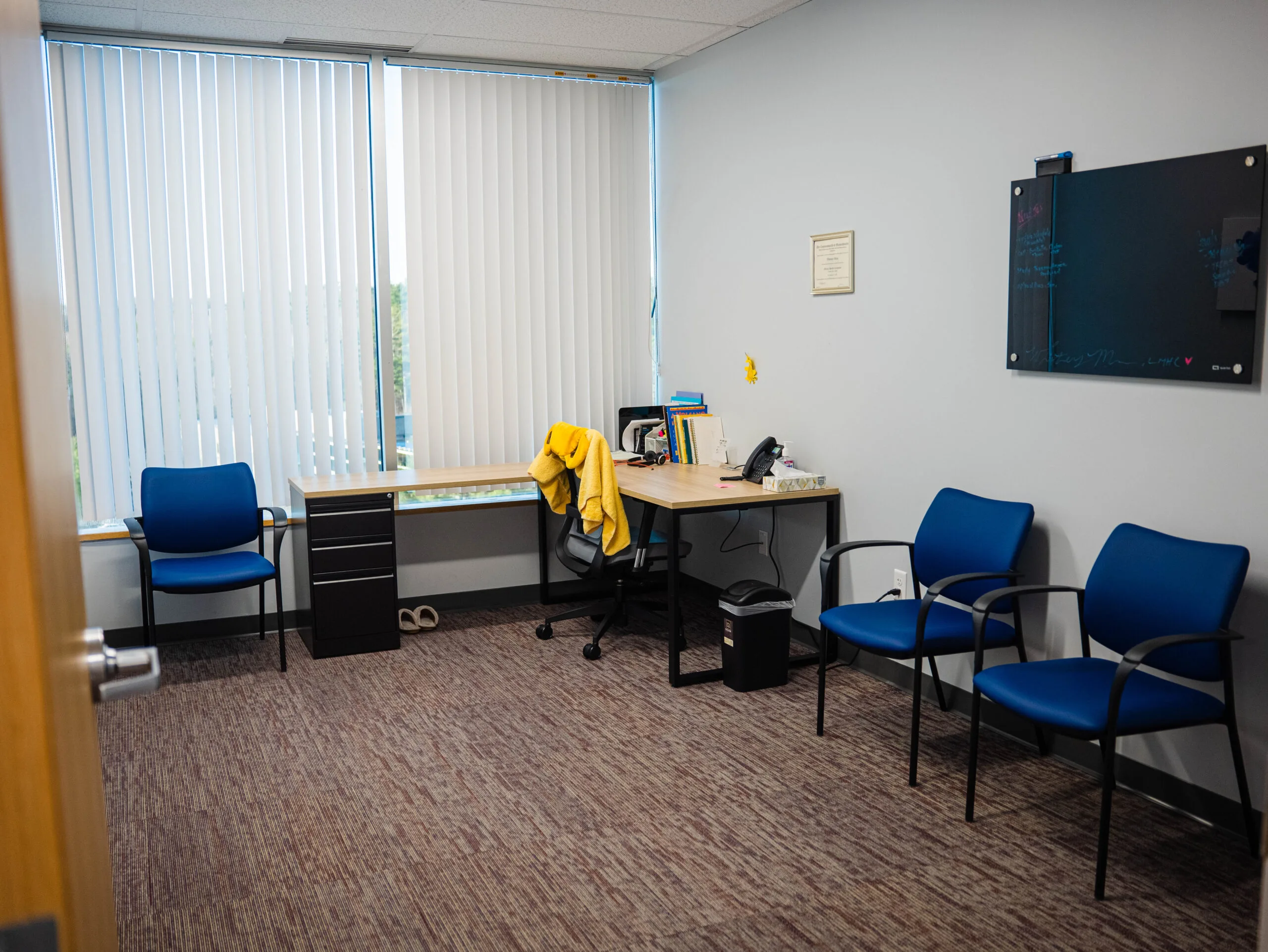 Office workspace with desk, computer, blue chairs, and windows with vertical blinds