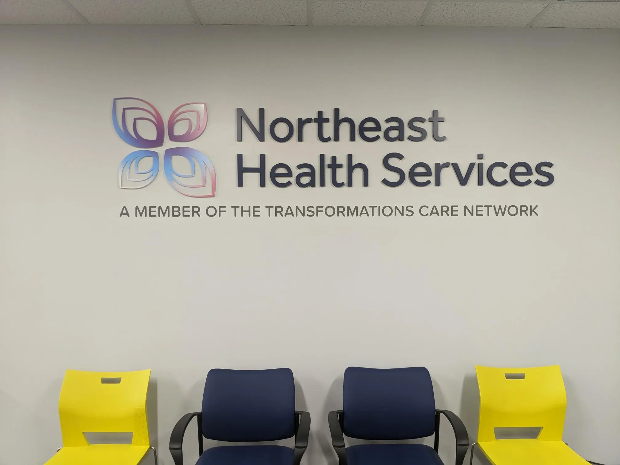 Northeast Health Services logo and text on waiting room wall with yellow and blue chairs