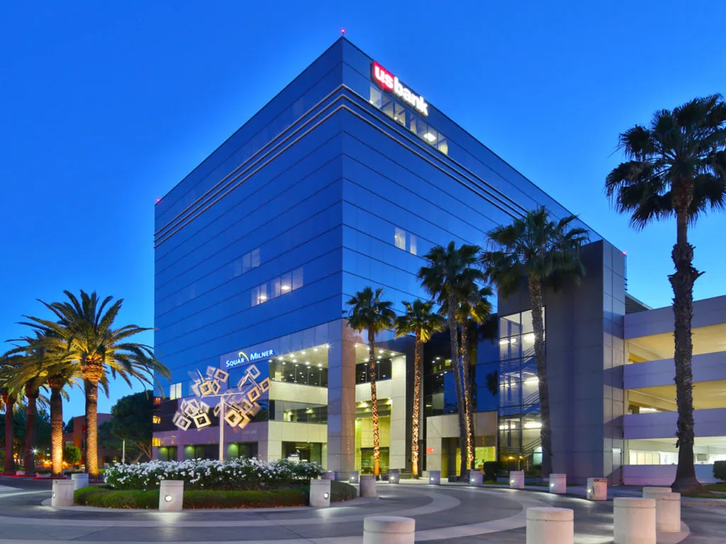 Modern medical building exterior at dusk with blue glass facade and palm trees