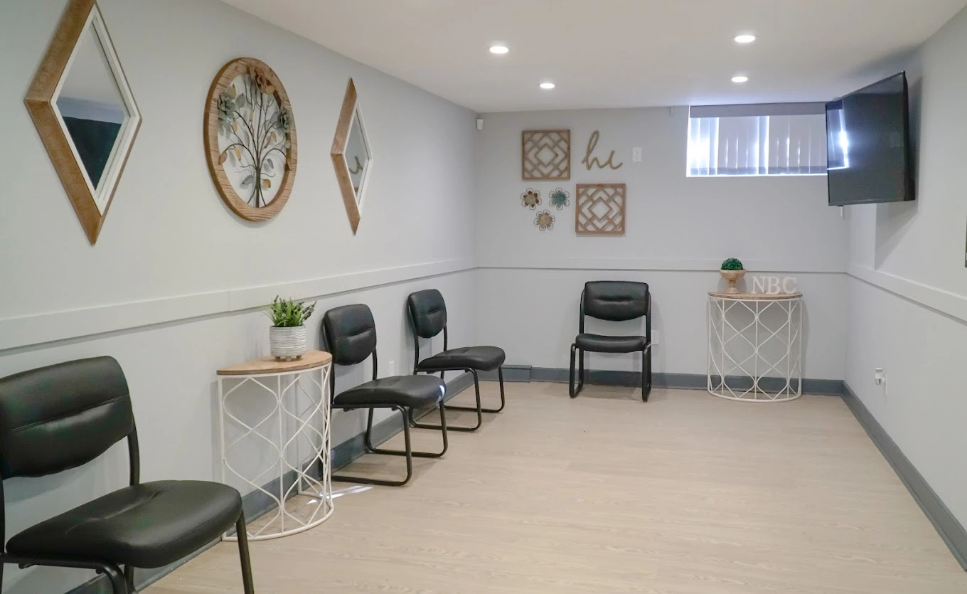 TMS therapy office waiting room with black chairs, white side tables with plants, decorative wall art, and TV screen