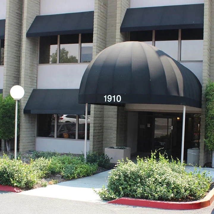 Building entrance at 1910 with black dome awning, dark windows, and landscaped shrubs