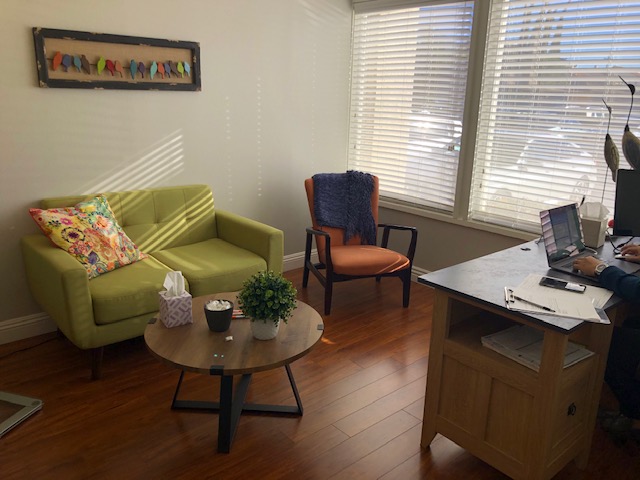 Consultation room with lime-green armchair, orange-upholstered chair, round coffee table, and wooden desk