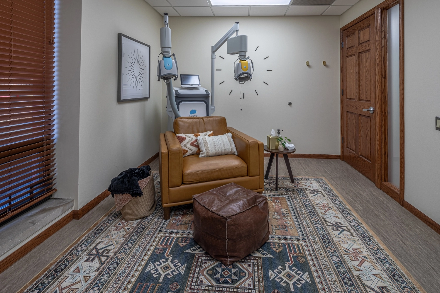 Treatment room with TMS therapy device mounted overhead, brown leather chair, and ottoman seating