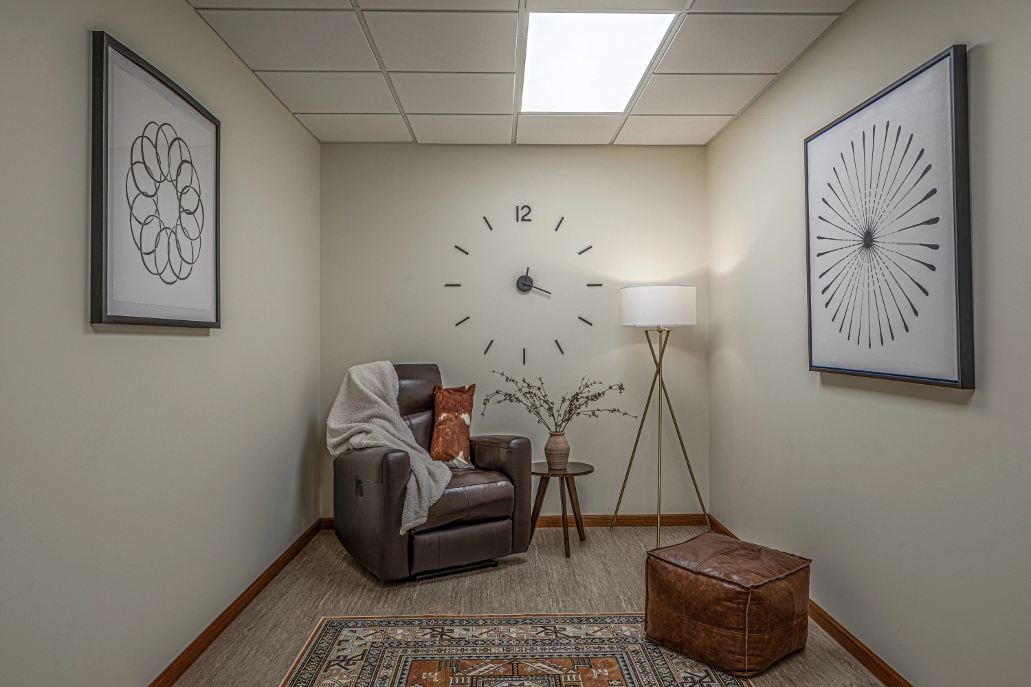 Small therapy space with dark leather recliner, tripod lamp, wall art, and brown ottoman