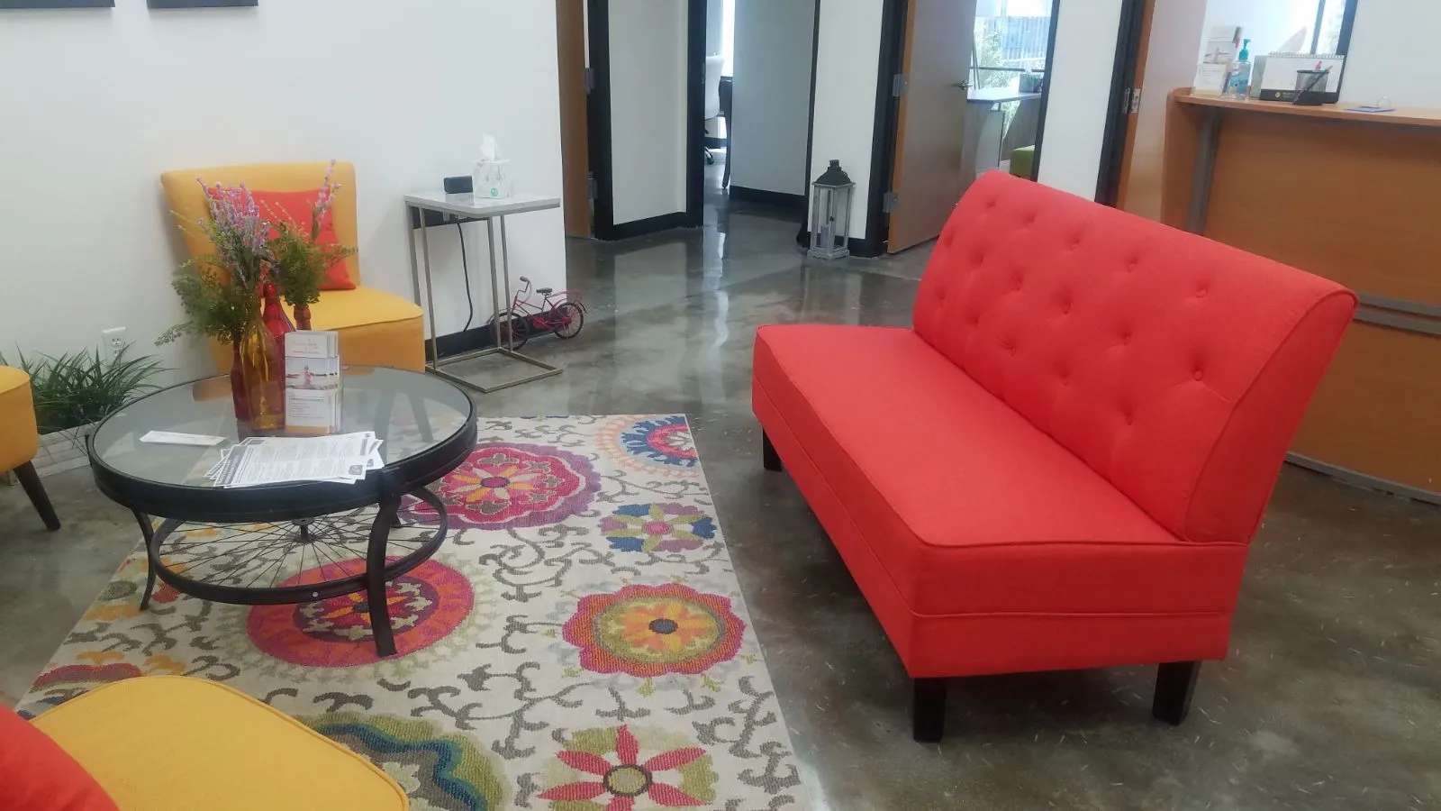 TMS therapy clinic waiting room with red sofa, yellow chair, round black table, and colorful area rug