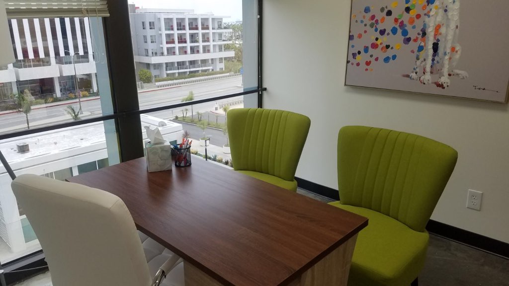 Conference room with dark wood table, green chairs, abstract colorful artwork, and view of urban buildings