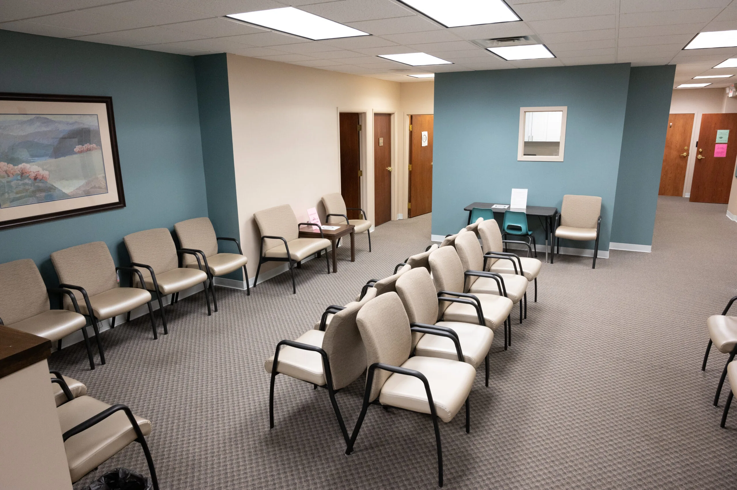 TMS therapy clinic lobby with blue and tan walls, multiple padded chairs arranged in rows, and wood doors leading to treatment areas