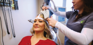Clinician applying TMS treatment headpiece to patient wearing red shirt in clinical setting