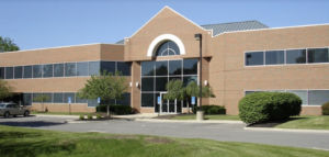 Single-story brick medical building with round window, columns at entrance, and parked cars
