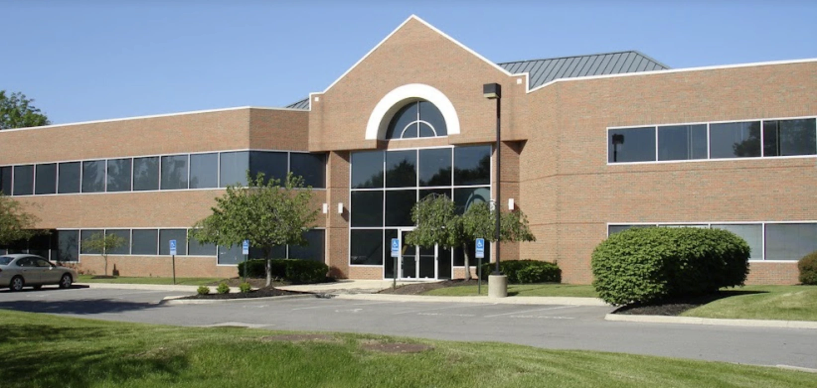 Single-story brick medical building with round window, columns at entrance, and parked cars