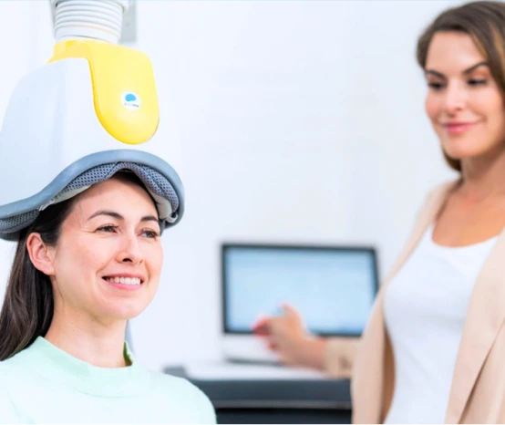 Patient wearing yellow and blue TMS treatment coil on head during therapy session
