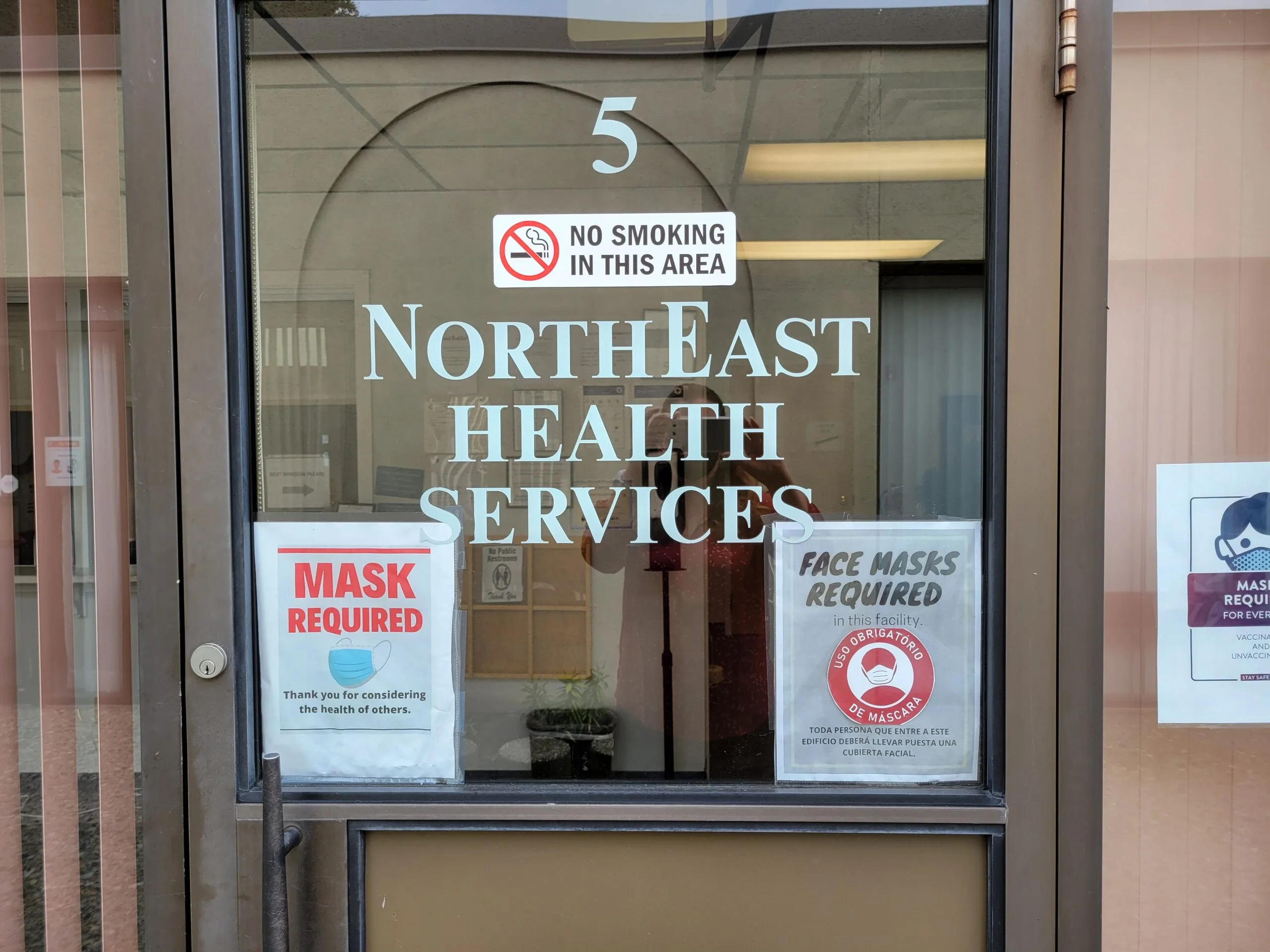 Glass entrance door with NorthEast Health Services signage, no smoking sign, and mask required notices