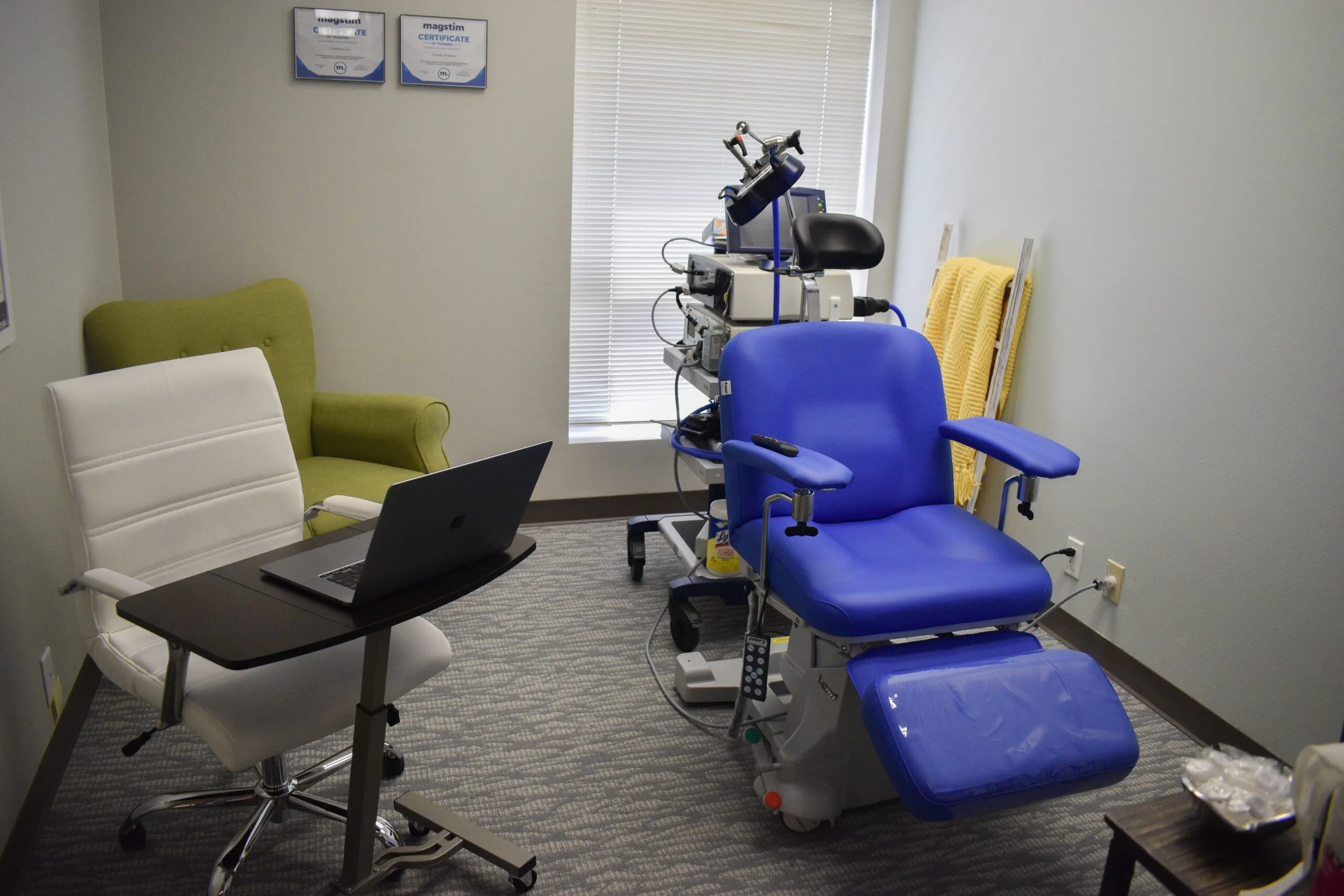 Westlake TMS room with blue treatment chair, robotic TMS device mounted overhead, and clinician workspace