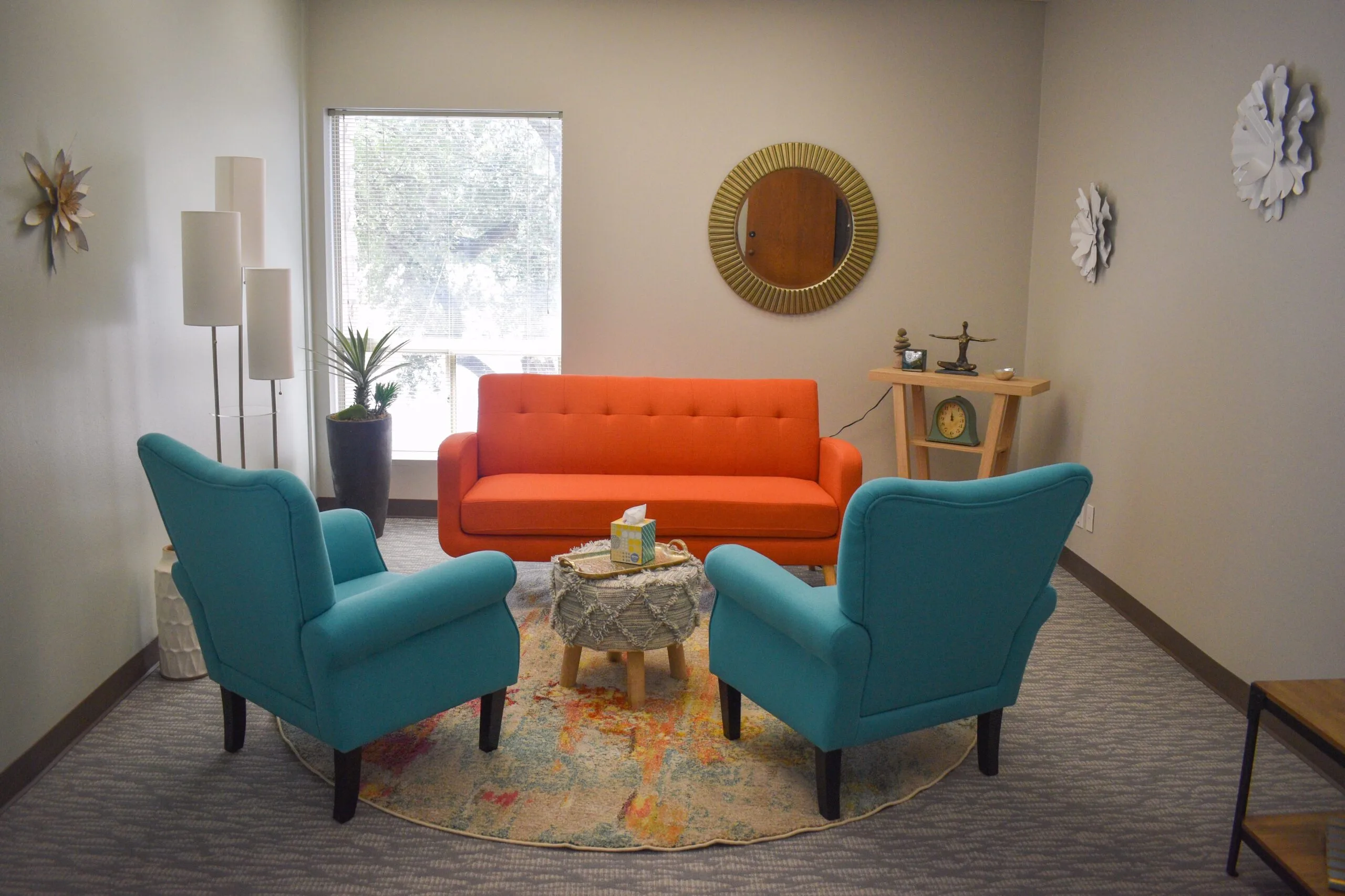 Westlake therapy room with teal armchairs, orange sofa, and brass-framed mirror in calming interior