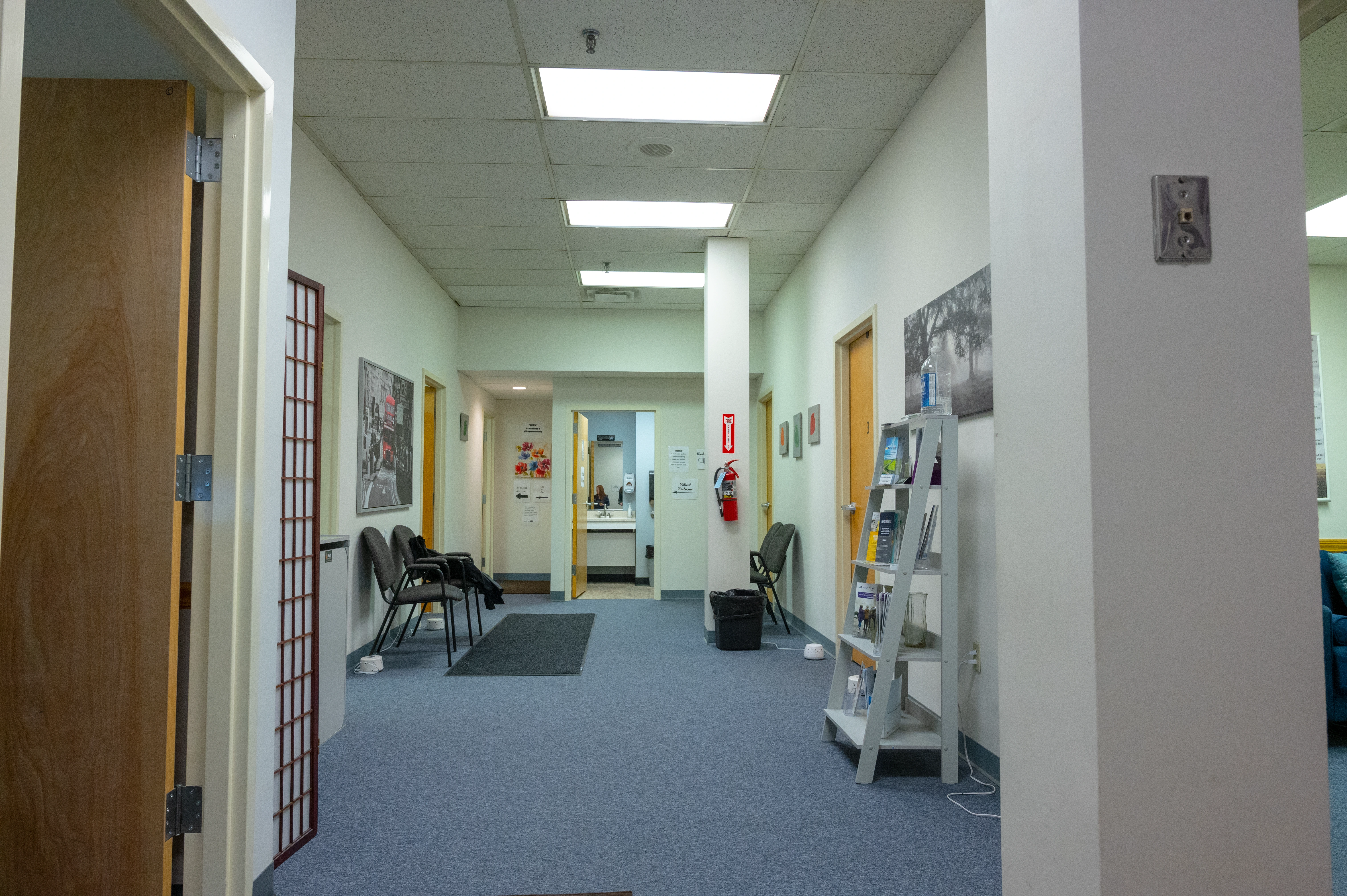 Clinic hallway with blue carpet, treatment room doors, and informational materials on walls