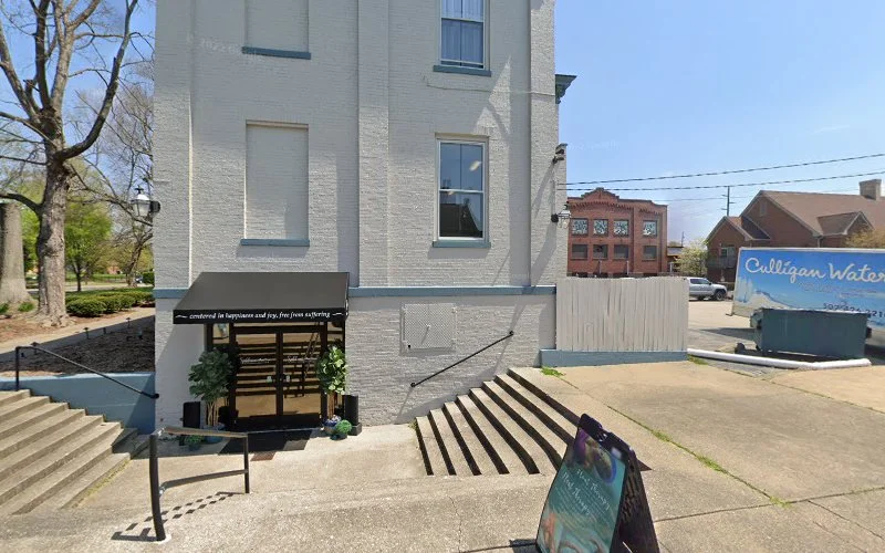 Exterior of white brick building with entrance ramp and stairs, bare tree, and neighboring brick building on sunny day