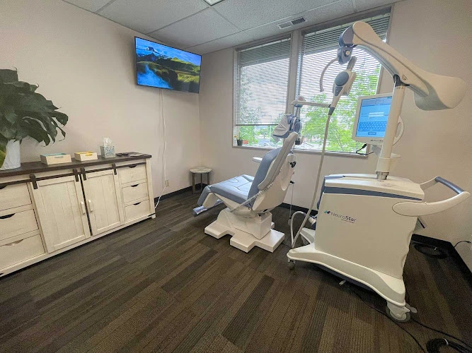 Clinical treatment room with TMS device, patient chair, wall-mounted monitor, and wooden storage cabinetry