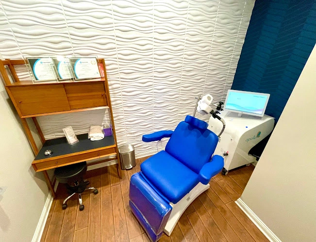 TMS treatment room with blue patient chair, computer monitor, and wooden bookshelf against textured wall