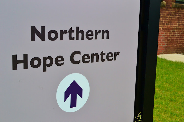 Northern Hope Center sign with upward arrow logo on building exterior with brick wall and lawn visible