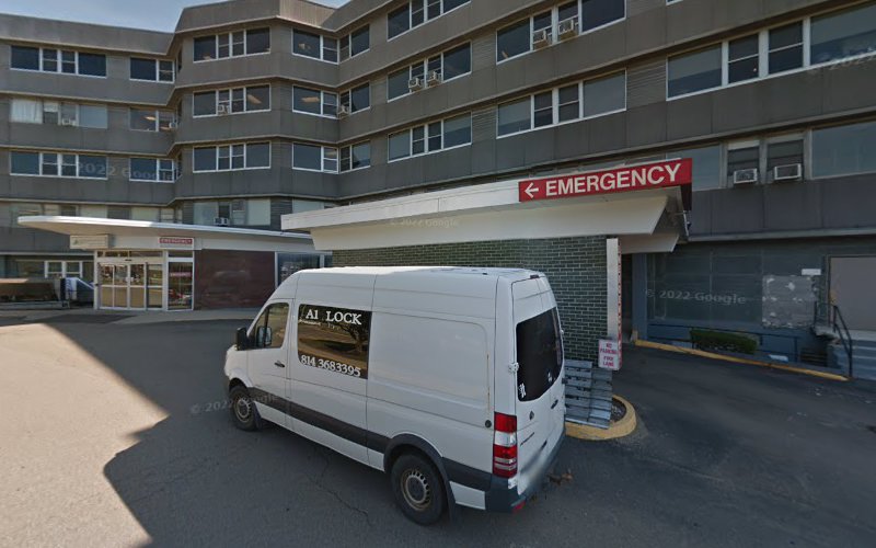 White service van parked at hospital emergency entrance with multi-story brick building behind