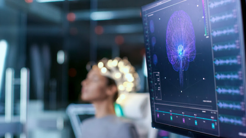 Patient wearing TMS coil headpiece during treatment while brain scan displays on monitor