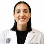 Caitlin Strebing, clinical professional wearing white coat over black shirt, smiling at camera
