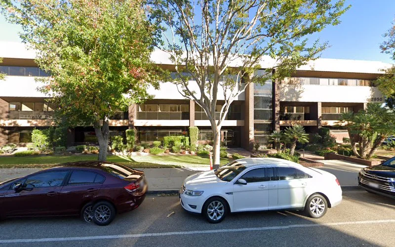 Modern medical building exterior with multi-level architecture, large tree, and parked cars in front driveway