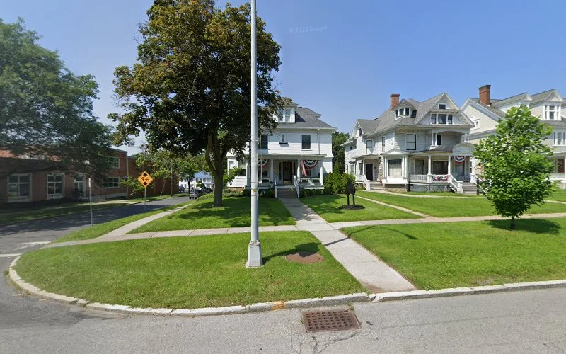 Tree-lined residential street with white Victorian homes and brick building in Canandaigua