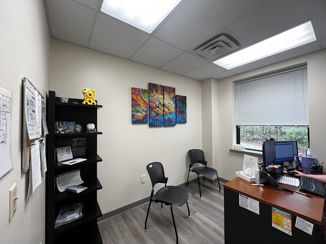 Clinical office with desk, two chairs, black shelving unit, and colorful artwork on wall