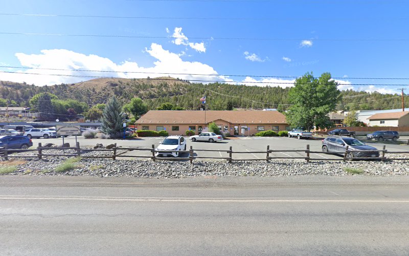 Single-story brown brick building with parking lot and wooden fence, mountains in background