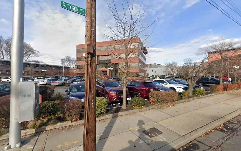 Street corner showing S Tyson Ave sign, brick building, and parking lot with multiple vehicles
