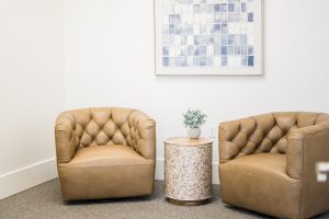 Waiting room with two tan leather armchairs, small table with plant, and framed artwork