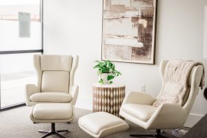 Welcoming reception area with two cream wingback chairs, ottoman, and potted plant on wooden side table
