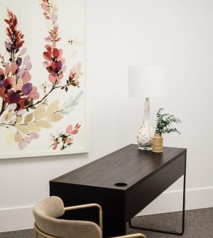 Black desk with decorative vase and plant beside framed botanical artwork with red and pink flowers