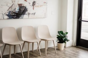 Three cream modern chairs facing large window with potted green plant and abstract wall art