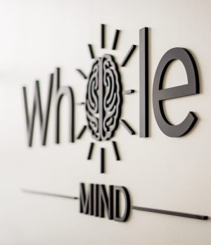 Whole Mind logo with brain illustration and radiating lines on wall