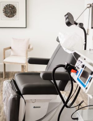 TMS therapy treatment chair with overhead lamp, control panel, and comfortable waiting chair in background