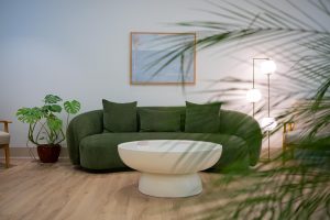 Modern waiting room with green curved sofa, white table, potted plants, and framed artwork
