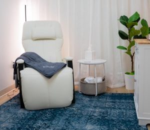 TMS treatment chair with Stella branded blanket, side table, and potted plant in clinical room