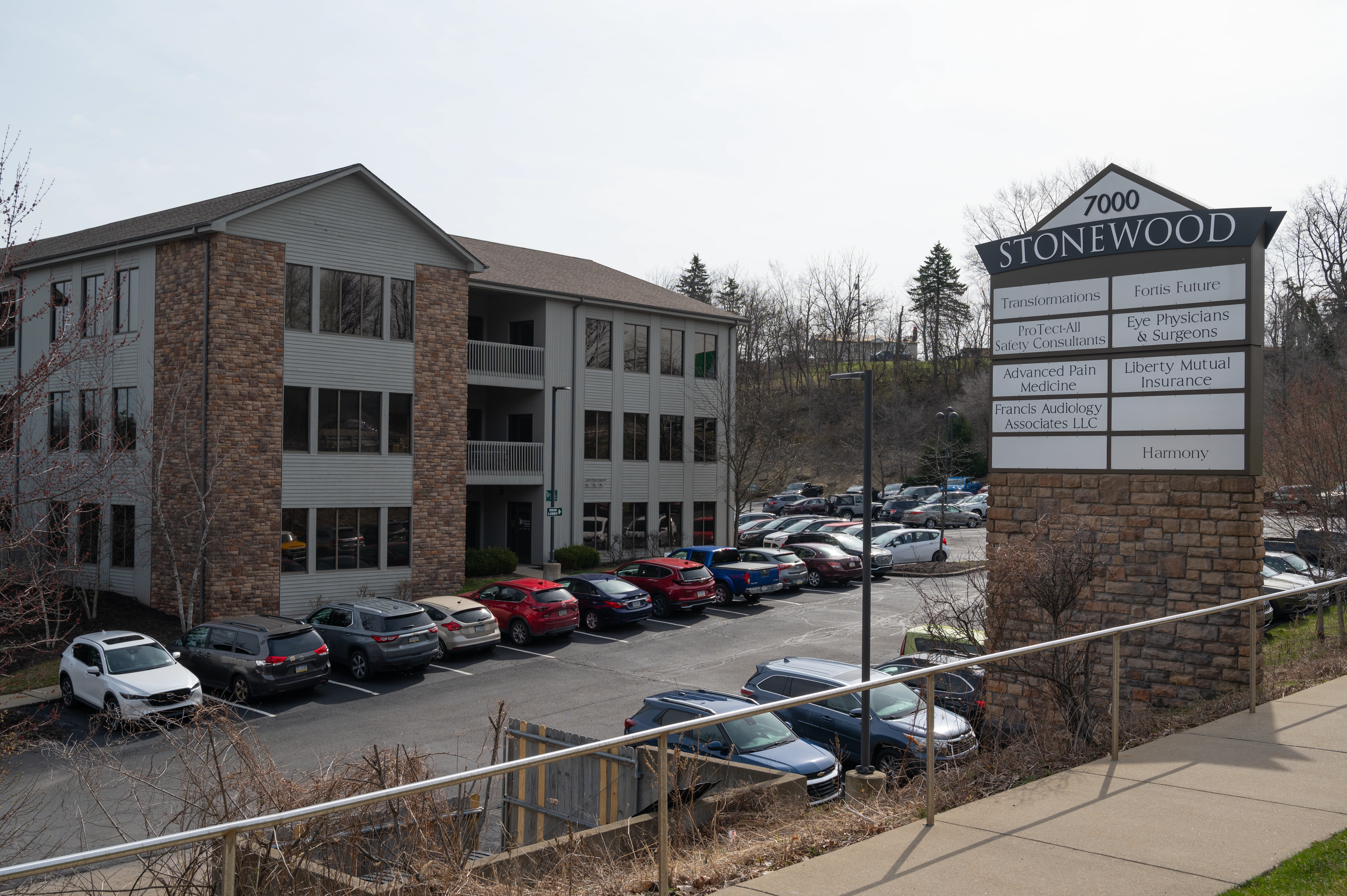 Stonewood building exterior with brick and siding, parked cars in lot, and directional sign listing multiple medical practices