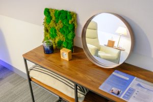 Wooden desk with decorative moss wall panel, round mirror, small plant in container, and blue accent lighting below