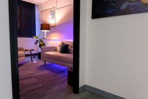 Modern therapy office lounge with purple ambient lighting, gray sofa, table lamp, and plant
