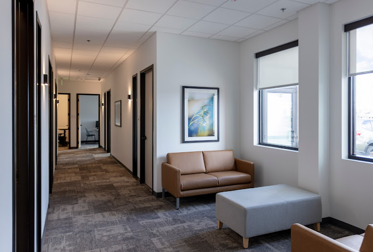 Parker clinic waiting area with brown sofa, gray ottoman, framed artwork, and corridor with treatment room doors