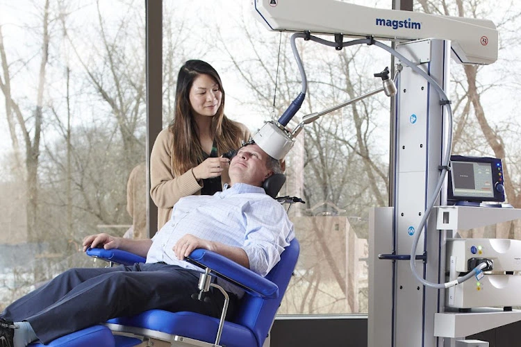 Clinician administering Magstim TMS treatment to patient seated in medical chair